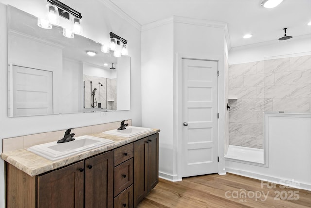 bathroom with ornamental molding, vanity, a tile shower, and wood-type flooring