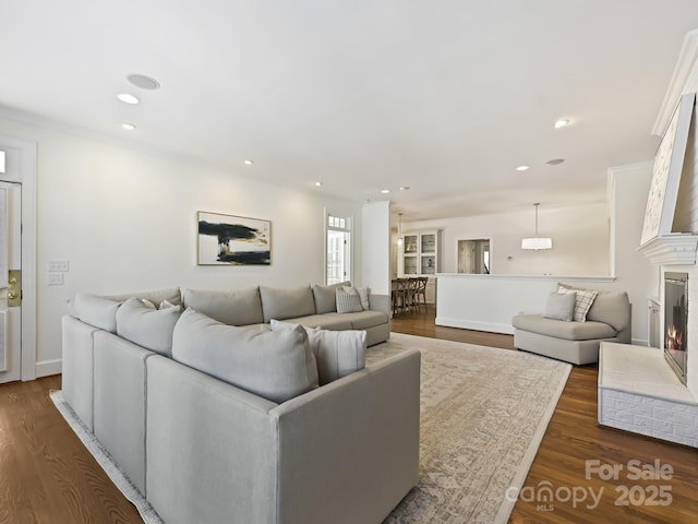 living area with dark wood-style floors, recessed lighting, and a warm lit fireplace