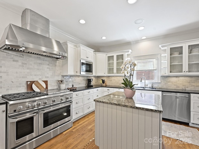 kitchen with a center island, appliances with stainless steel finishes, glass insert cabinets, white cabinets, and wall chimney range hood