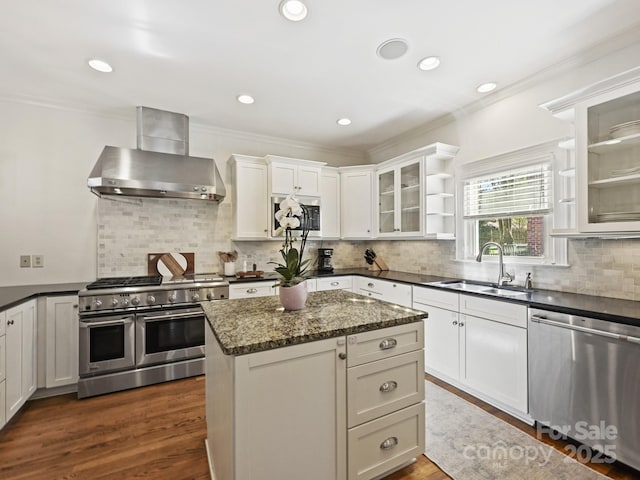 kitchen featuring glass insert cabinets, appliances with stainless steel finishes, wall chimney range hood, open shelves, and a sink