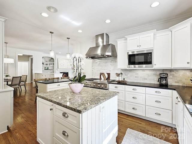 kitchen featuring black microwave, wall chimney exhaust hood, a kitchen island, and pendant lighting