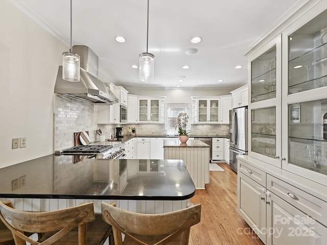 kitchen with stainless steel appliances, white cabinets, hanging light fixtures, range hood, and glass insert cabinets