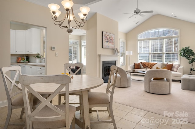 dining space with light tile patterned floors, lofted ceiling, a fireplace, ceiling fan with notable chandelier, and light colored carpet