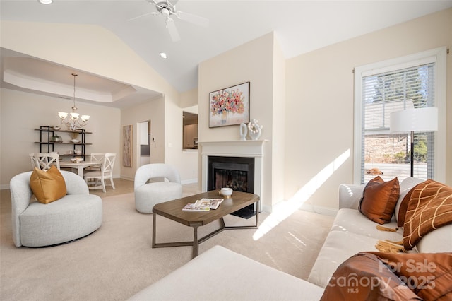 living room with baseboards, lofted ceiling, ceiling fan with notable chandelier, a fireplace, and a raised ceiling