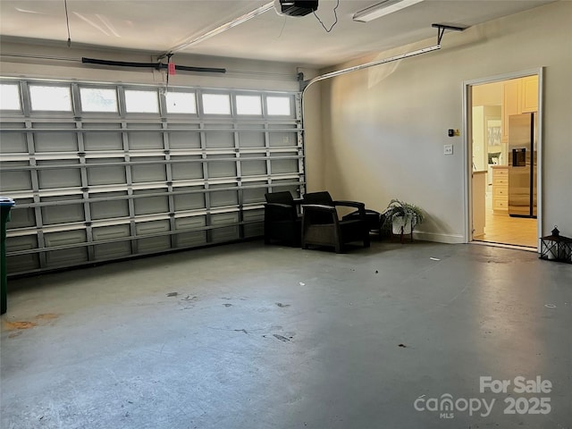 garage with a garage door opener and stainless steel refrigerator with ice dispenser