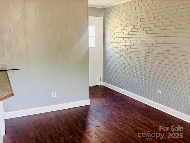 spare room featuring crown molding, dark wood-type flooring, and brick wall