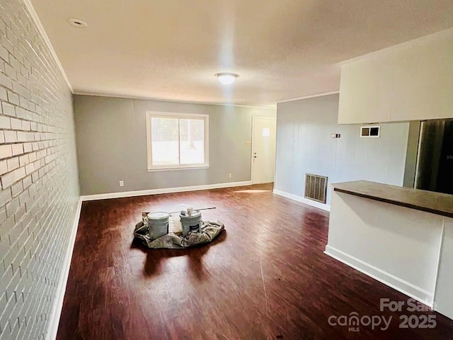 unfurnished living room featuring crown molding, brick wall, a textured ceiling, and hardwood / wood-style flooring