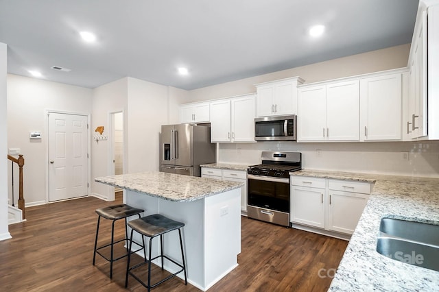 kitchen with light stone counters, dark wood-type flooring, white cabinetry, appliances with stainless steel finishes, and a center island