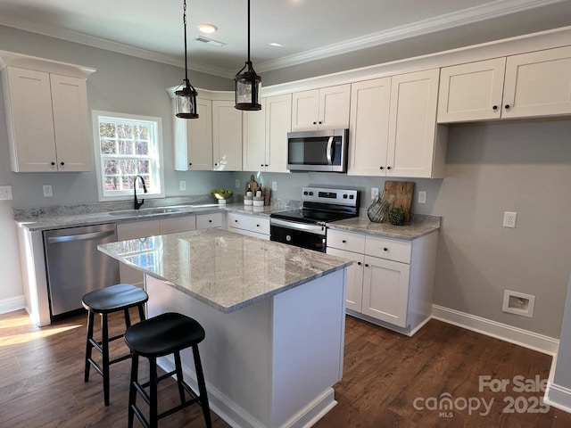 kitchen featuring white cabinets, appliances with stainless steel finishes, a center island, crown molding, and a sink