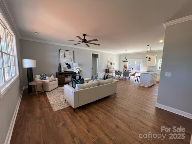 living area featuring dark wood-style floors, baseboards, ornamental molding, and a ceiling fan