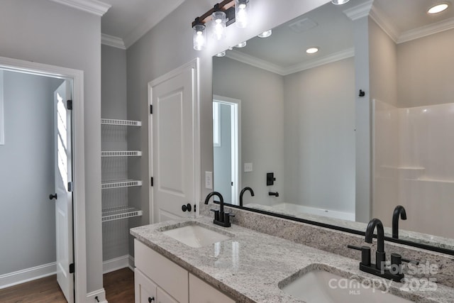 full bath with double vanity, wood finished floors, a sink, and crown molding