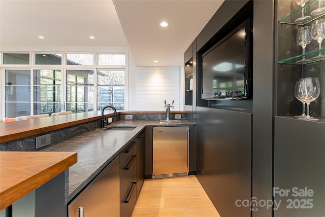 kitchen featuring light wood finished floors, stainless steel fridge, dark stone counters, a sink, and recessed lighting