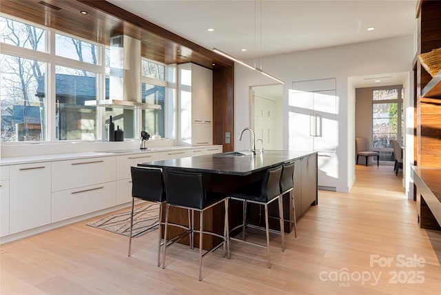 kitchen with modern cabinets, island exhaust hood, a kitchen bar, white cabinetry, and a sink