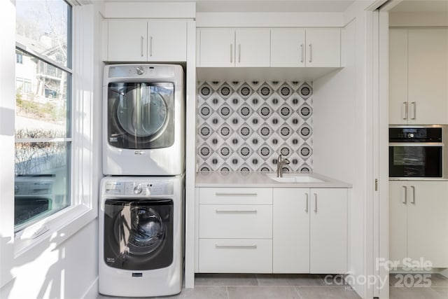 laundry room with a sink, light tile patterned floors, and stacked washer / dryer