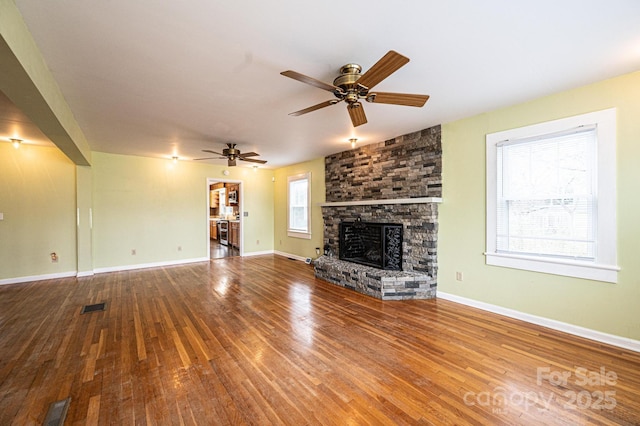 unfurnished living room with a stone fireplace, wood finished floors, visible vents, and baseboards