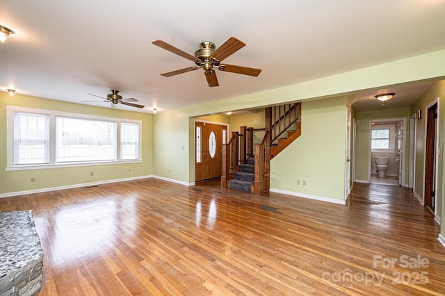 unfurnished living room with ceiling fan, stairs, baseboards, and wood finished floors