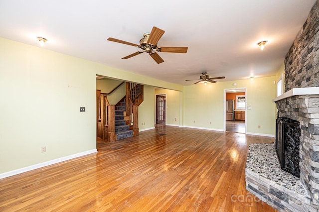 unfurnished living room featuring light wood-style flooring, a large fireplace, stairway, and baseboards