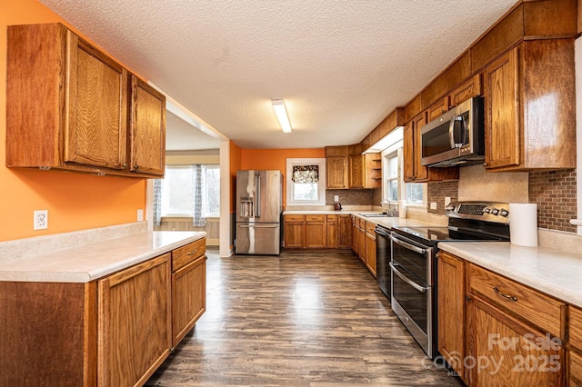 kitchen with stainless steel appliances, dark wood-style flooring, brown cabinetry, and a sink