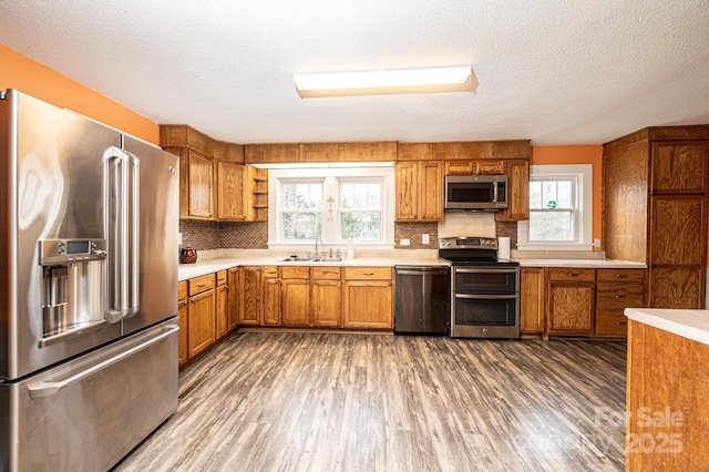 kitchen with brown cabinetry, stainless steel appliances, a sink, and wood finished floors