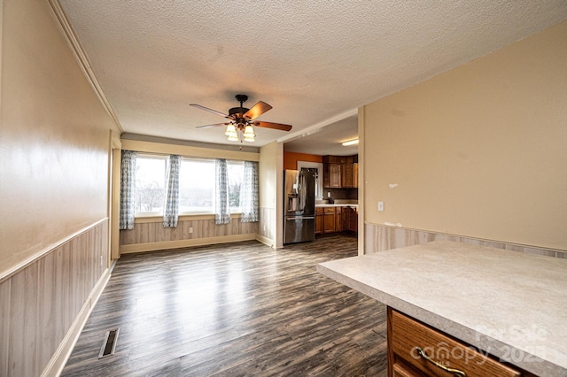 kitchen featuring brown cabinetry, a wainscoted wall, dark wood-style flooring, a textured ceiling, and stainless steel refrigerator with ice dispenser