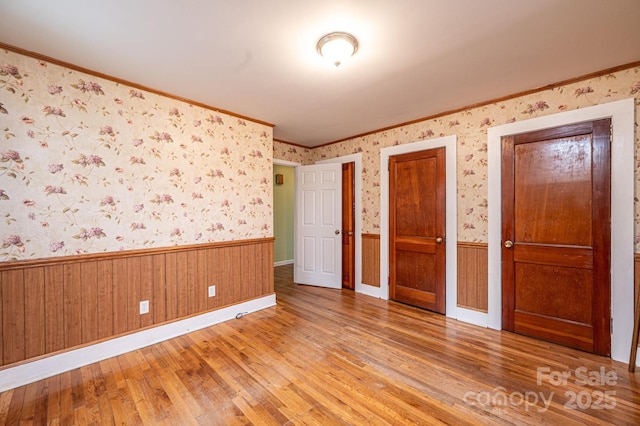 unfurnished bedroom with hardwood / wood-style flooring, a wainscoted wall, crown molding, and wallpapered walls