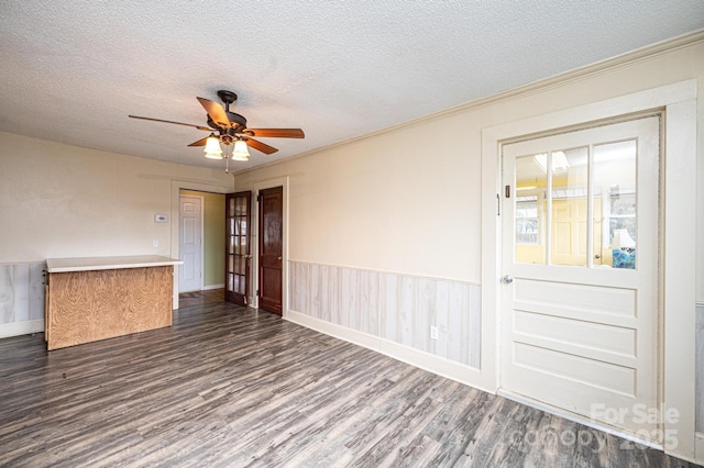 empty room with a wainscoted wall, dark wood-type flooring, a textured ceiling, and a ceiling fan