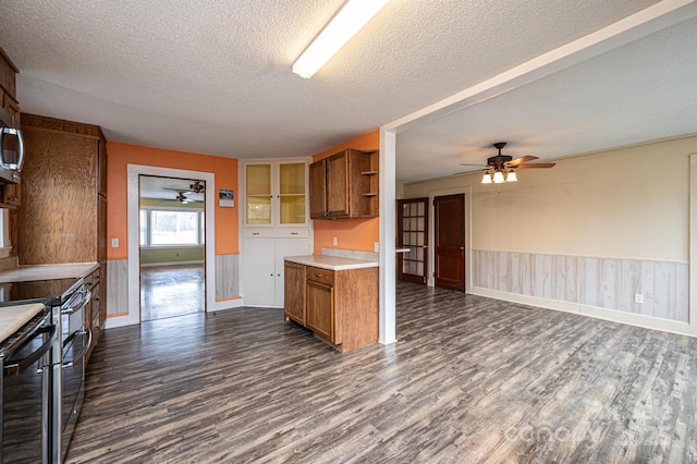 kitchen with stainless steel appliances, brown cabinetry, wainscoting, and dark wood-style flooring