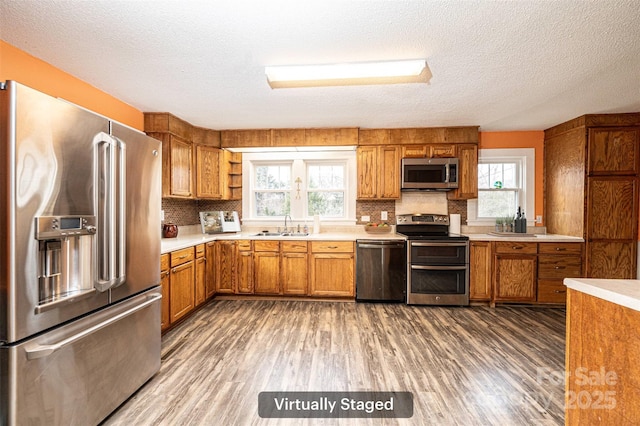 kitchen featuring light countertops, appliances with stainless steel finishes, brown cabinetry, a sink, and wood finished floors