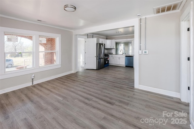 unfurnished living room featuring wood finished floors, a sink, visible vents, and crown molding