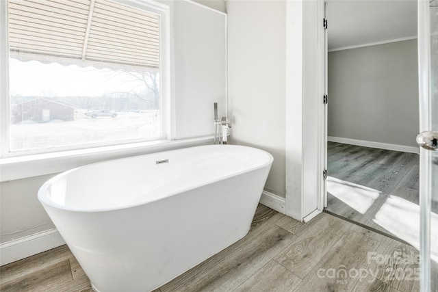 full bath featuring a freestanding tub, baseboards, ornamental molding, and wood finished floors