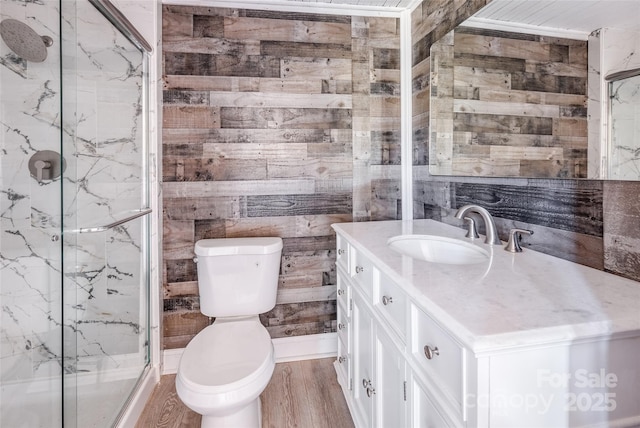 bathroom with toilet, wooden walls, wood finished floors, vanity, and a marble finish shower