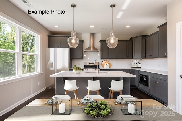 kitchen with wall chimney range hood, white fridge with ice dispenser, a sink, healthy amount of natural light, and recessed lighting