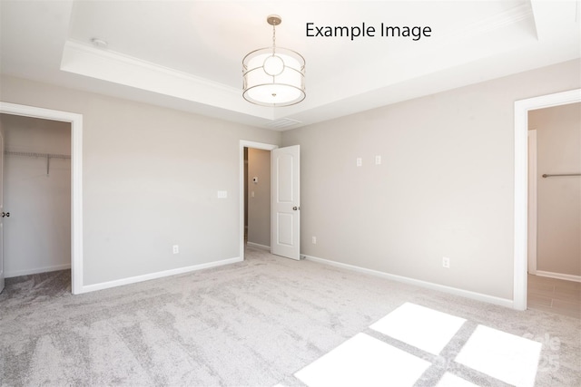 unfurnished bedroom with a raised ceiling, crown molding, carpet, a walk in closet, and baseboards