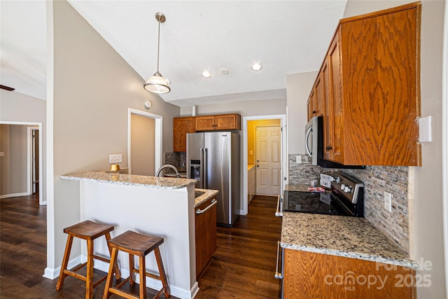 kitchen featuring appliances with stainless steel finishes, brown cabinets, dark wood-style flooring, a peninsula, and vaulted ceiling