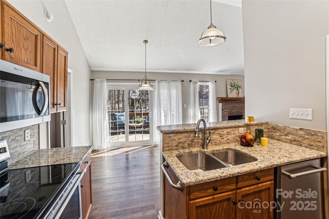 kitchen featuring a sink, vaulted ceiling, appliances with stainless steel finishes, brown cabinets, and dark wood finished floors