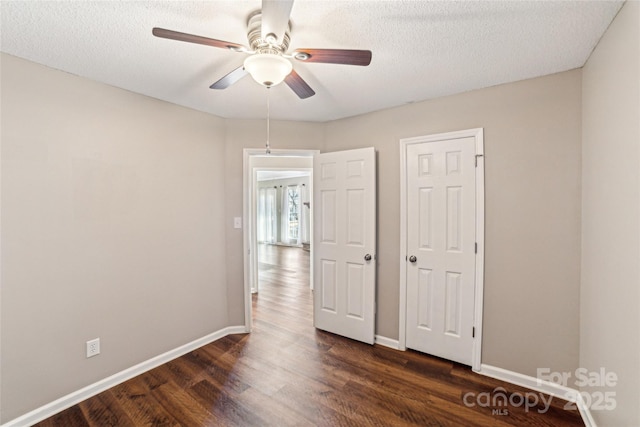 empty room with ceiling fan, a textured ceiling, baseboards, and dark wood-style flooring