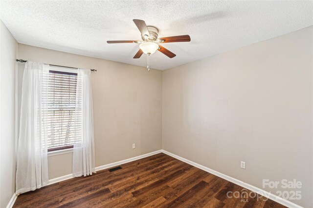 spare room featuring dark wood-type flooring, a wealth of natural light, a textured ceiling, and baseboards