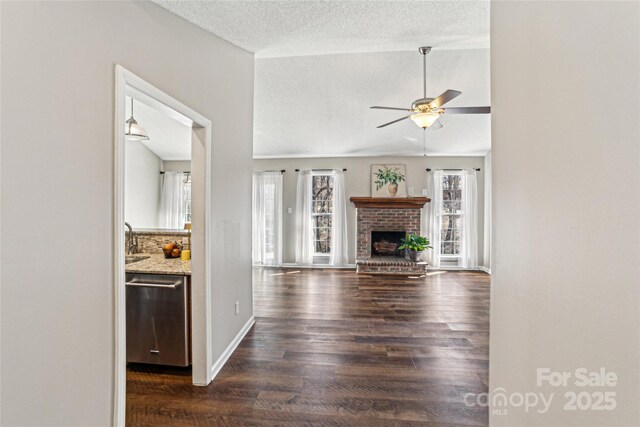 unfurnished living room with a ceiling fan, lofted ceiling, dark wood-style floors, a textured ceiling, and a fireplace