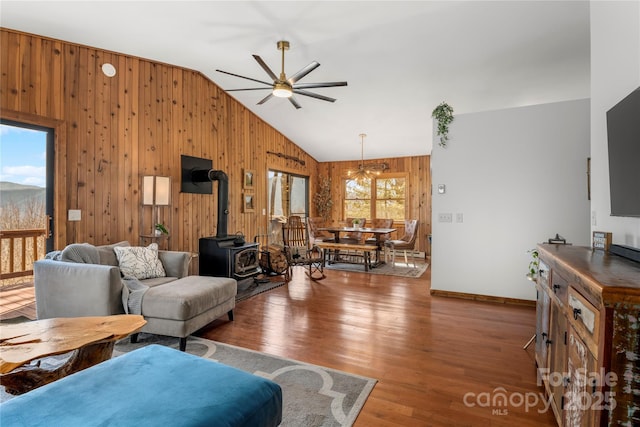 living room featuring wooden walls, lofted ceiling, ceiling fan, wood finished floors, and a wood stove