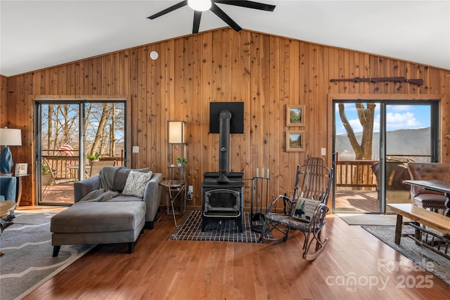 living area featuring vaulted ceiling, wood-type flooring, a wood stove, and wooden walls