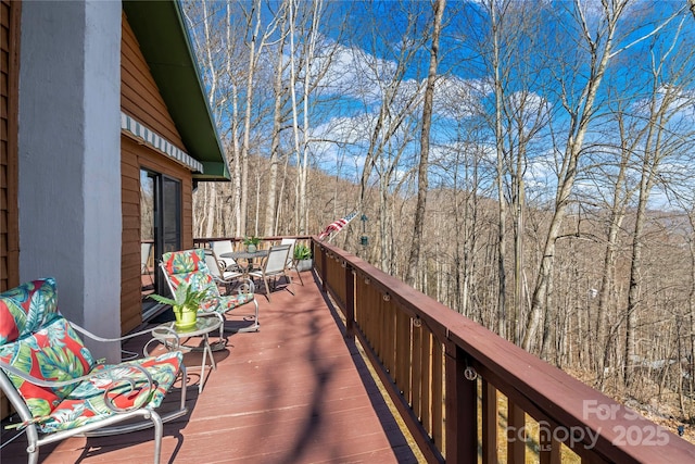 wooden deck with a forest view and outdoor dining space