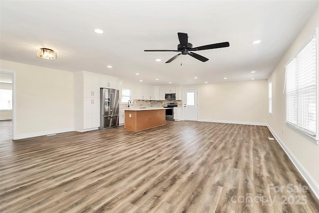 unfurnished living room with plenty of natural light, baseboards, a sink, and light wood finished floors