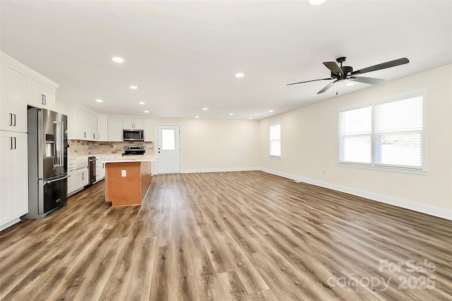 kitchen with white cabinets, a kitchen island, open floor plan, stainless steel appliances, and light countertops