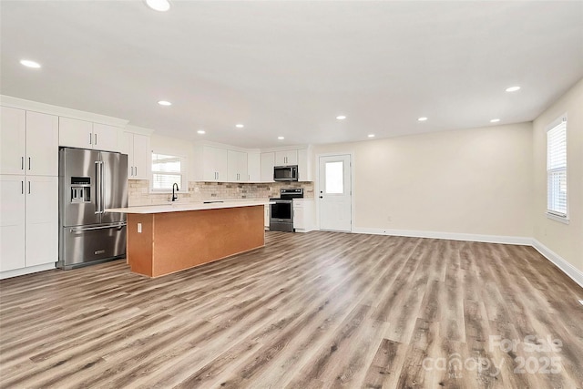 kitchen with stainless steel appliances, a kitchen island, white cabinets, open floor plan, and light countertops