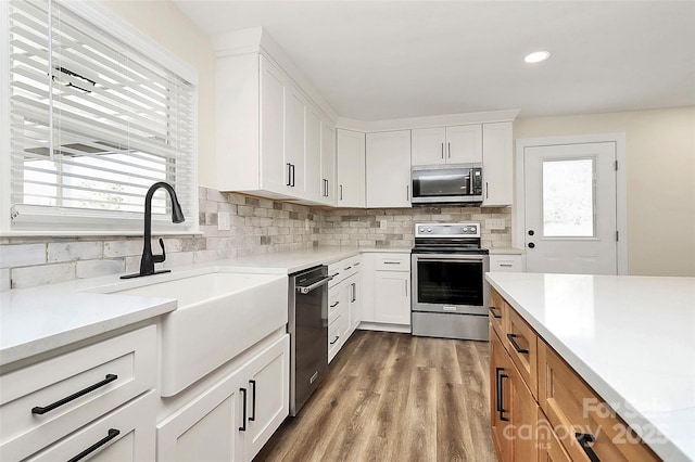 kitchen with wood finished floors, a sink, white cabinetry, appliances with stainless steel finishes, and decorative backsplash