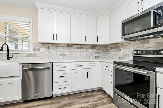 kitchen with wood finished floors, a sink, white cabinetry, light countertops, and appliances with stainless steel finishes