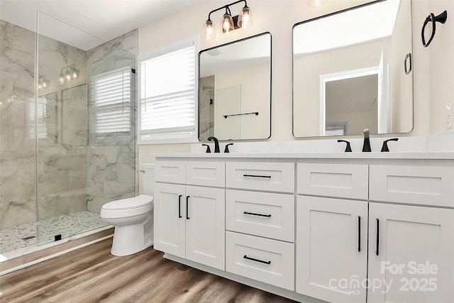 bathroom featuring double vanity, tiled shower, toilet, wood finished floors, and a sink