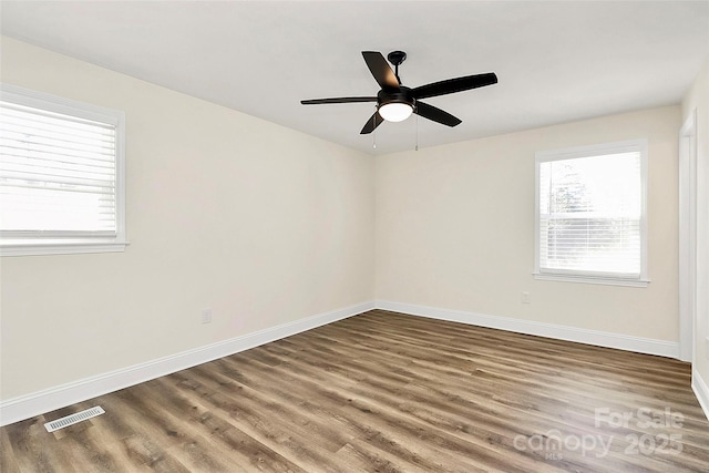 unfurnished room featuring dark wood-style floors, visible vents, baseboards, and a ceiling fan