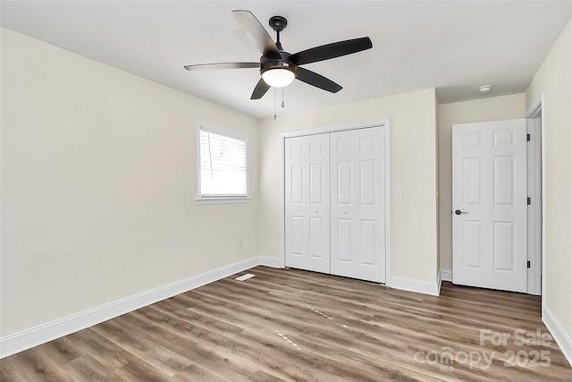 unfurnished bedroom featuring ceiling fan, a closet, baseboards, and wood finished floors