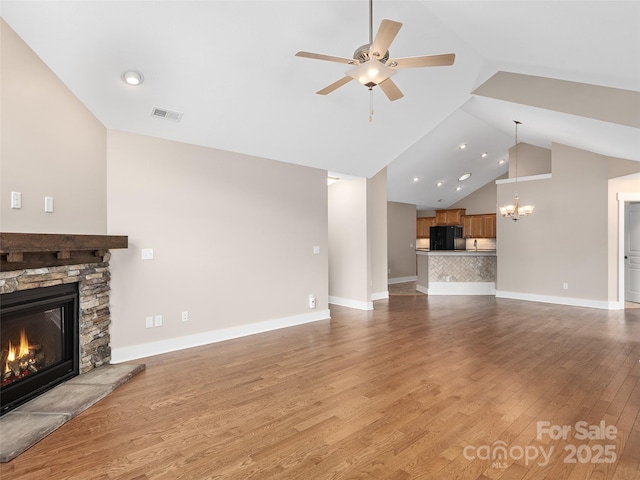 unfurnished living room with a stone fireplace, hardwood / wood-style floors, ceiling fan with notable chandelier, and high vaulted ceiling